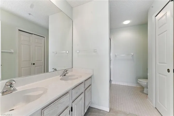 Bathroom with a closet, a textured ceiling, double vanity, a shower stall, and light tile patterned floors