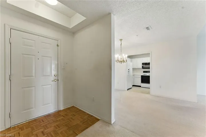 Foyer with a textured ceiling, a chandelier, and light carpet