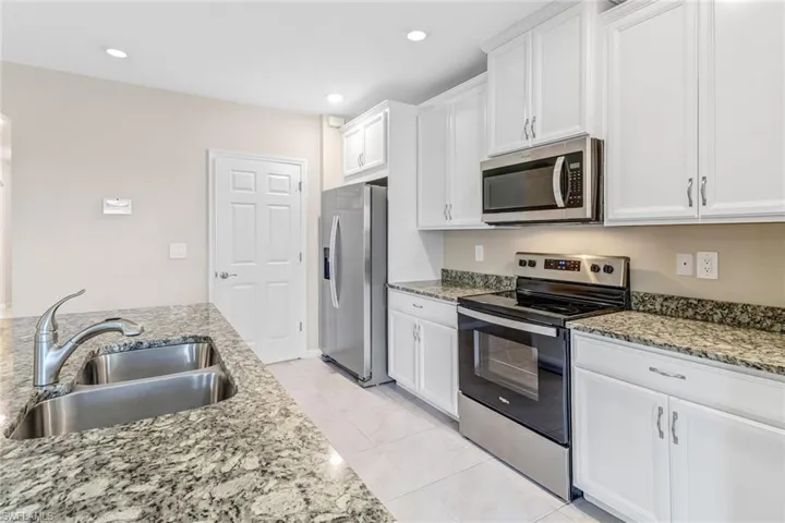 Kitchen featuring light stone countertops, stainless steel appliances, light tile flooring, sink, and white cabinetry