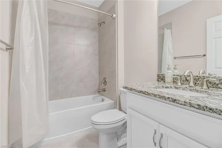Full bathroom with shower / bath combo with shower curtain, oversized vanity, toilet, and tile floors