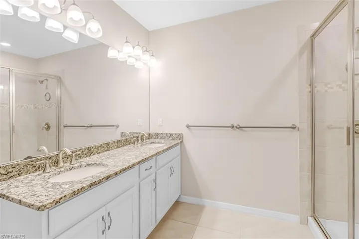 Bathroom featuring tile flooring, dual sinks, a shower with door, and large vanity