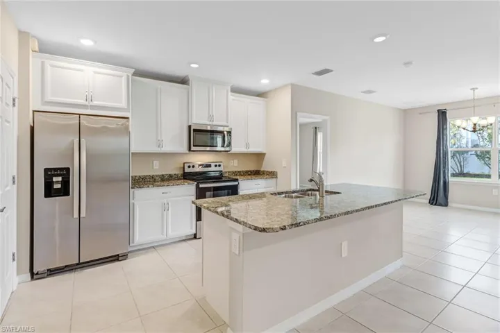 Kitchen featuring light tile flooring, an island with sink, white cabinets, sink, and appliances with stainless steel finishes
