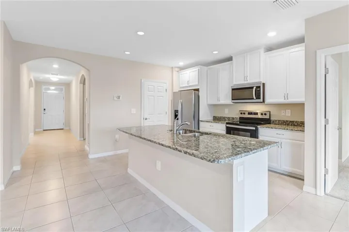 Kitchen featuring an island with sink, stainless steel appliances, white cabinets, and sink