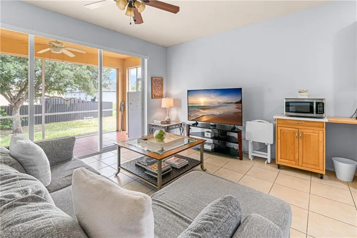Tiled flooring throughout, screened patio with ceiling fan, backyard with mature trees, and a built-in wood-finish cabinet with a countertop