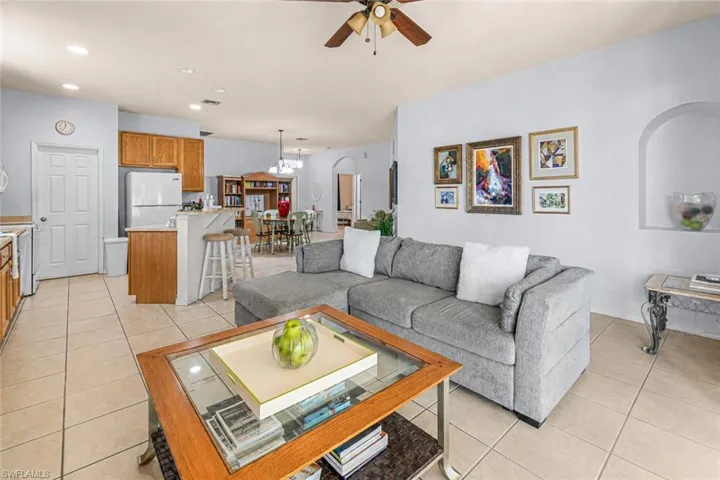 Light-toned tile flooring, recessed lighting, ceiling fan, kitchen with wood cabinetry and a breakfast bar, and an arched wall niche