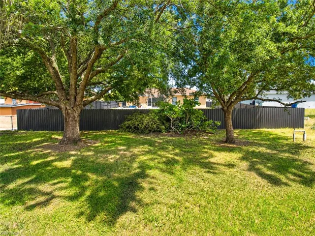 Expansive yard with mature trees, green lawn, and a dark privacy fence