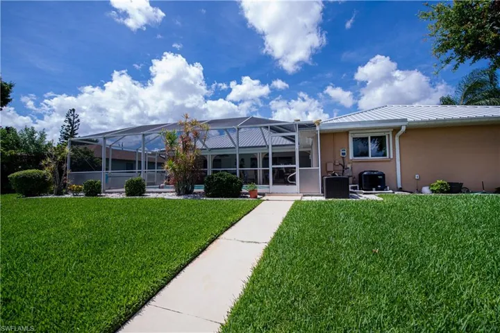 Rear view of house featuring screen enclosure, central AC, and a yard
