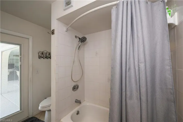 Bathroom with tile floors, shower / bath combination with curtain, plenty of natural light, and toilet with pool acces