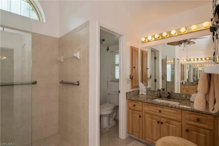 Bathroom featuring tiled shower, tile flooring, two seperate vanities, seperate toilet area, and lofted ceiling