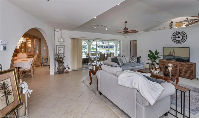 Living room with ceiling fan, lofted ceiling, and rail lighting, sliding glass doors leading out the the screened lanai and pool