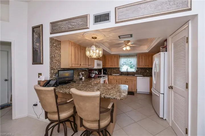Kitchen with ceiling fan, white appliances, tasteful granite countertop and backsplash, and a raised ceiling