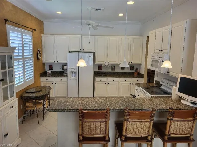 Kitchen with white appliances, light tile patterned floors, white cabinetry, a kitchen breakfast bar, and ornamental molding