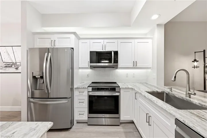 Kitchen featuring stainless steel appliances, light stone counters, and white cabinetry