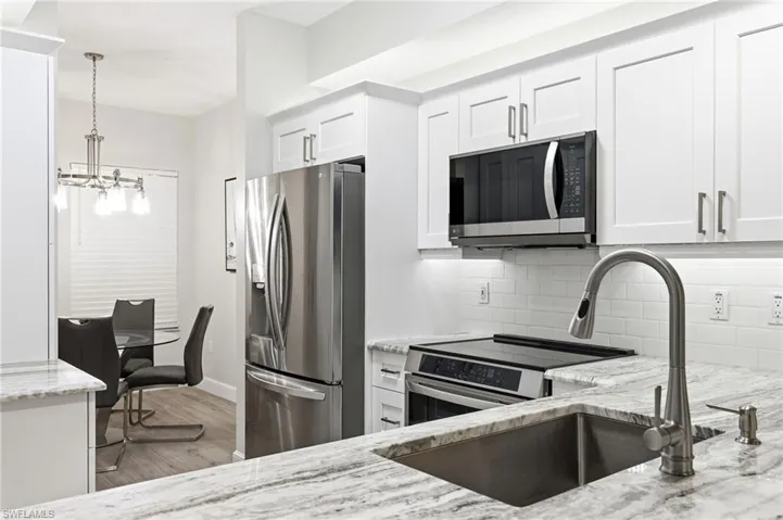 Kitchen with appliances with stainless steel finishes, light stone counters, white cabinets, decorative light fixtures, and a chandelier
