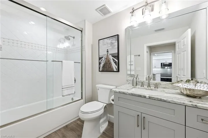 Bathroom featuring vanity, bath / shower combo with glass door, and dark wood finished floors