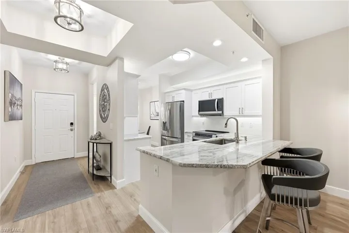 Kitchen featuring white cabinets, light stone counters, a peninsula, stainless steel appliances, and a kitchen bar
