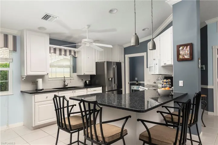 Kitchen featuring stainless steel fridge with ice dispenser, a sink, white microwave, light tile patterned floors, and a peninsula