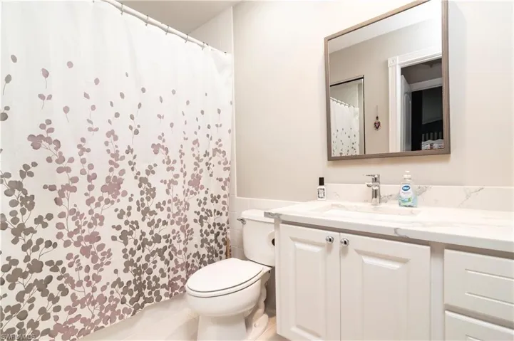 Full bath with toilet, vanity, a wainscoted wall, curtained shower, and tile walls