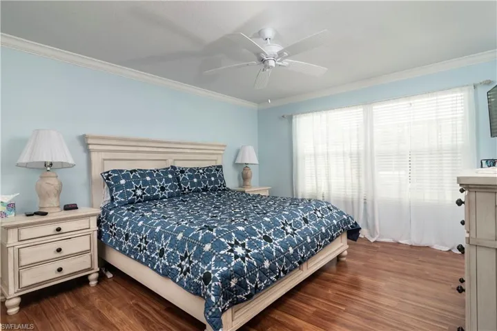 Bedroom with dark wood-style floors, crown molding, multiple windows, and a ceiling fan