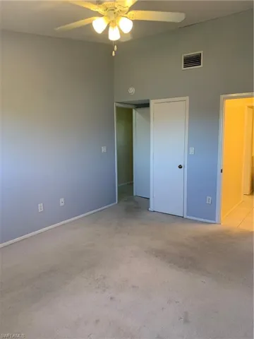 Bedroom featuring ceiling fan, a towering ceiling, light carpet, and a closet