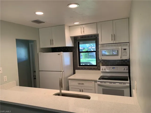 Kitchen featuring white appliances, white cabinets, sink, decorative backsplash, and light stone counters