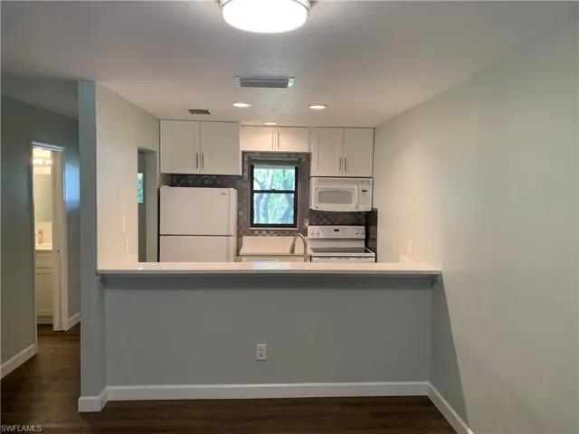 Kitchen with white appliances, sink, tasteful backsplash, dark hardwood / wood-style flooring, and white cabinetry