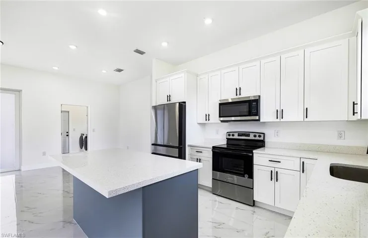Kitchen featuring a kitchen island, appliances with stainless steel finishes, light stone counters, and white cabinetry