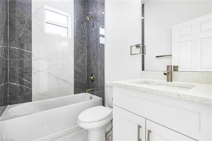 Full bathroom with tiled shower / bath, vanity, and toilet