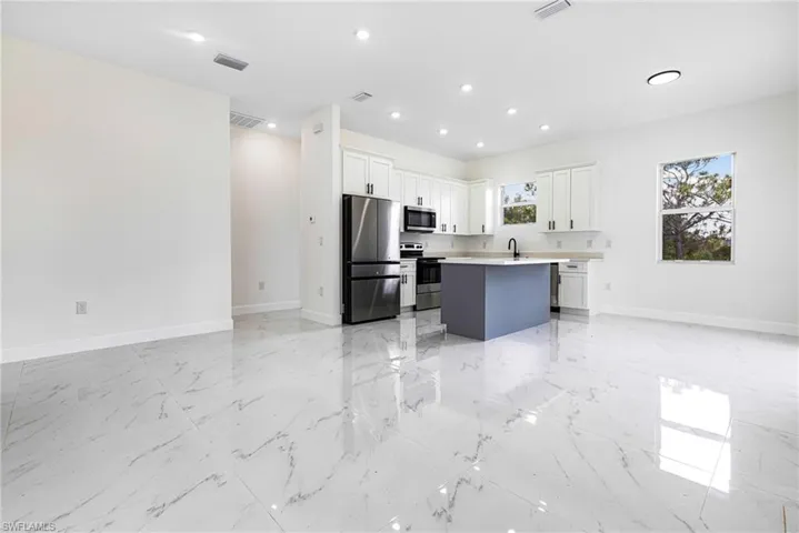 Kitchen with appliances with stainless steel finishes, white cabinetry, a center island, and sink