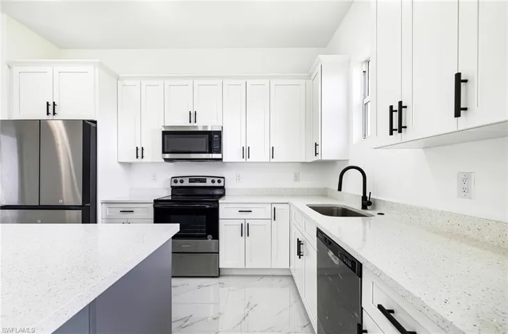 Kitchen featuring sink, white cabinets, light stone counters, and stainless steel appliances