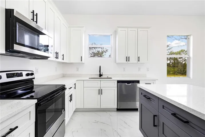 Kitchen featuring white cabinetry, light stone countertops, appliances with stainless steel finishes, and a wealth of natural light