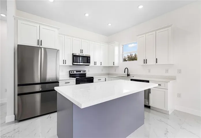 Kitchen with appliances with stainless steel finishes, white cabinets, a center island, and light stone counters