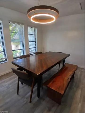 Dining area featuring a contemporary circular chandelier, wood-finish flooring, and multiple windows with blinds