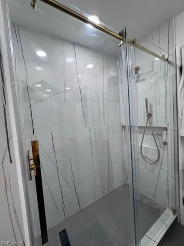Clear glass shower enclosure with a gold-tone sliding door system, featuring a gold-tone handle