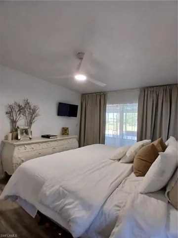 Bedroom featuring a contemporary ceiling fan with integrated lighting, wood-finish flooring, and a window with both sheer and blackout drapery