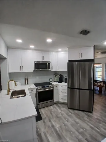 Modern kitchen featuring white shaker cabinetry, stainless steel appliances, a gold-finish faucet, white countertops, and wood-finish flooring