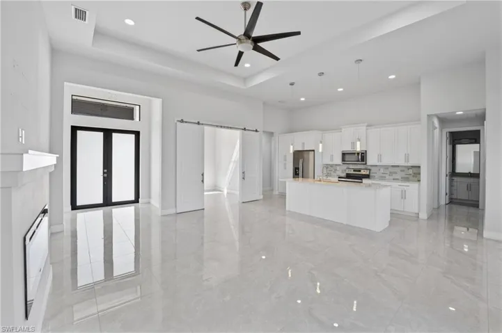 Kitchen featuring a barn door, white cabinetry, a tray ceiling, a ceiling fan, and an island with sink