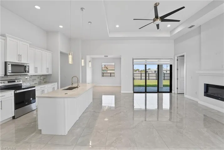 Kitchen with stainless steel appliances, white cabinetry, an island with sink, open floor plan, and a raised ceiling