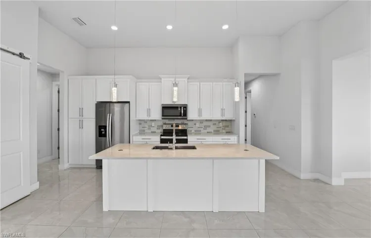 Kitchen featuring white cabinets, stainless steel appliances, a kitchen island with sink, light stone counters, and decorative backsplash