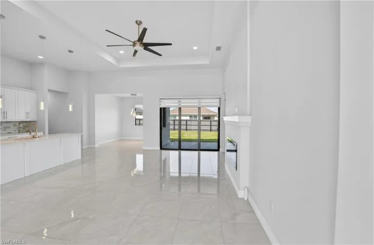 Unfurnished living room featuring a ceiling fan, recessed lighting, a tray ceiling, and light marble finish floors