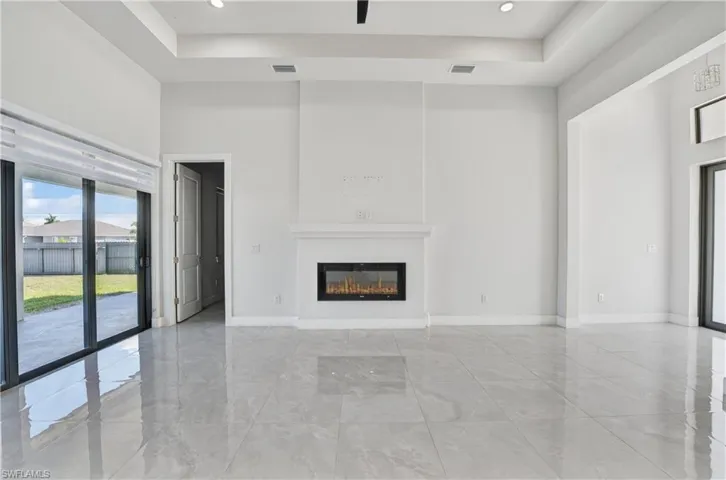 Unfurnished living room featuring a high tray ceiling, a glass covered fireplace, and recessed lighting