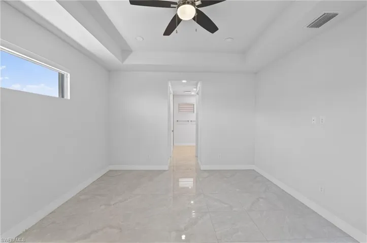 Empty room featuring a tray ceiling, a ceiling fan, recessed lighting, and light marble finish floors