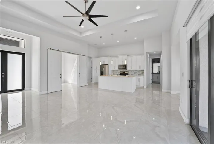 Unfurnished living room featuring a barn door, a ceiling fan, a tray ceiling, recessed lighting, and light marble finish flooring