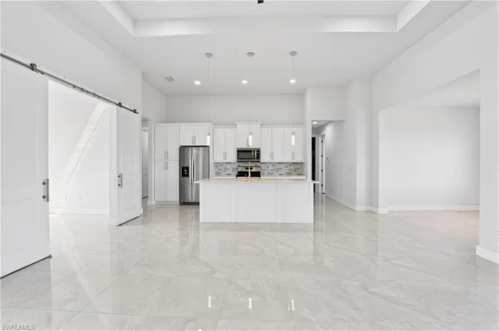 Kitchen with a barn door, open floor plan, white cabinets, stainless steel appliances, and a center island with sink