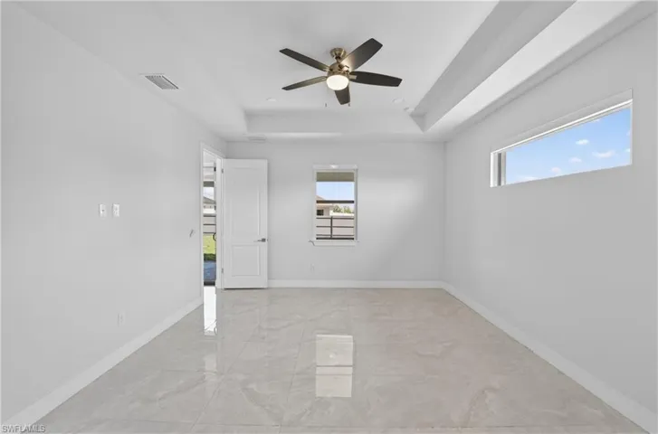 Empty room featuring a tray ceiling, ceiling fan, and light marble finish flooring
