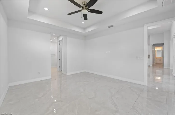 Empty room with a raised ceiling, recessed lighting, a ceiling fan, and light marble finish flooring