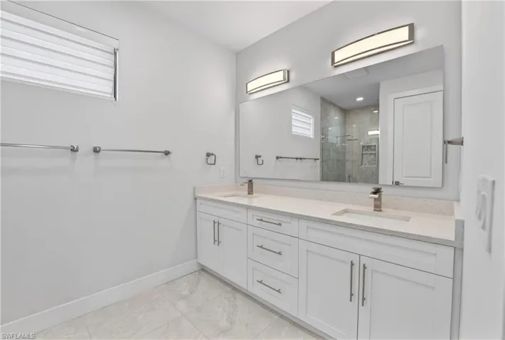 Bathroom with double vanity, a stall shower, and light marble finish floors