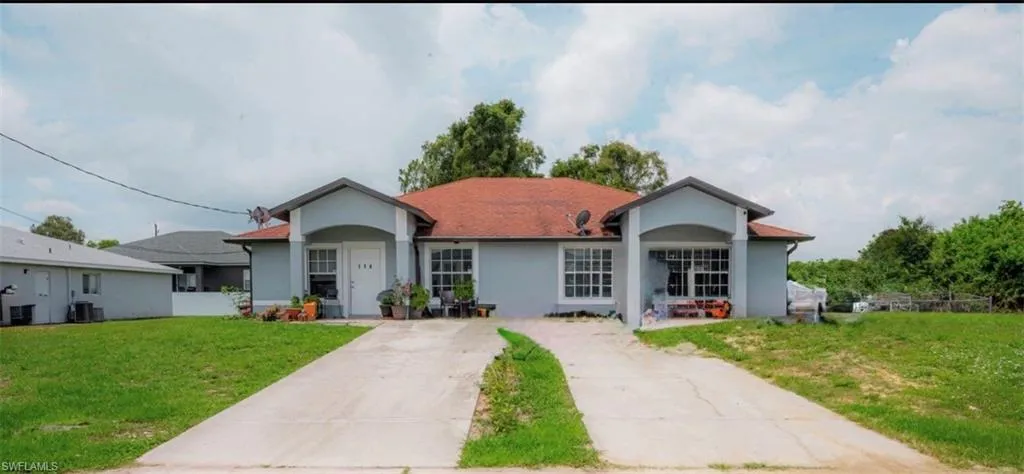 Duplex residence featuring a red tile roof, arched entryway details, light blue exterior siding, and separate paved driveways