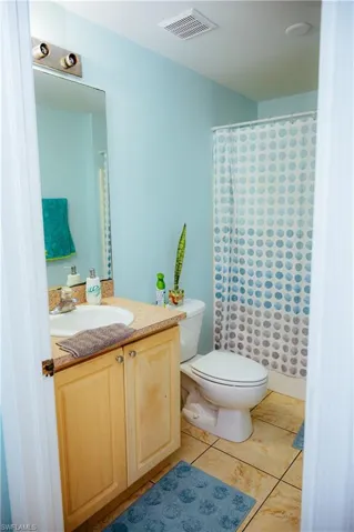 Bathroom featuring a vanity with a drop-in sink, a built-in toilet, and a shower with a curtain rod