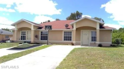 Duplex property with individual entrances and dedicated driveways, featuring a light-colored stucco exterior, prominent white trim, and a red-toned shingled roof